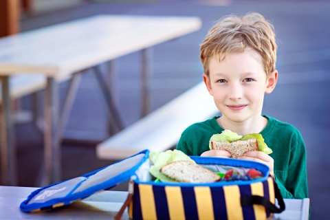 boy at school eating a sandwich from a lunch box