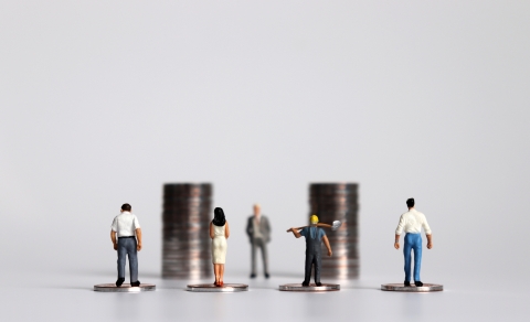 small people figurines standing in front of two piles of coins with their backs to the camera