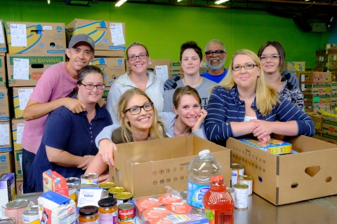 A group of volunteers with two boxes in front of them with food scattered on the table