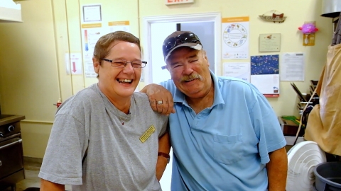 A man and women laughing with the mans arm resting on the women shoulder