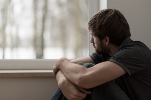 Man holding his knees looking out a window