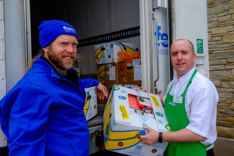 Two men holding boxes of food one wearing a Feed Nova Scotia attire and one a Sobey's uniform