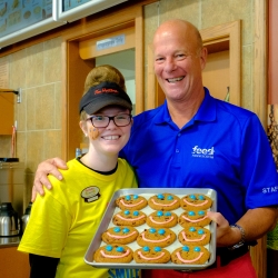 two people smiling holding a tray of chocolate chunk cookies