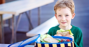 boy at school eating a sandwich from a lunch box