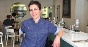 Restaurant owner smiling and leaning on the bar at her establishment