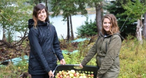 two women holding a tote full of apples