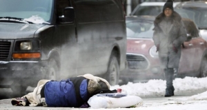 A pedestrian walks near a sleeping homeless person.