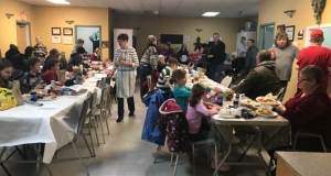 many people sitting at long tables eating a Christmas dinner