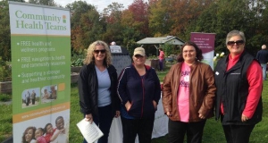 Four people standing in a garden next to a banner that says Community Health Teams