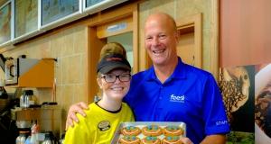 two people smiling holding a tray of chocolate chunk cookies