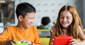 Two children smiling and looking into their lunchboxes in what looks like a classroom