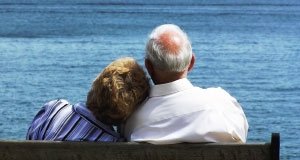 a senior couple sitting close on a bench in front of the ocean